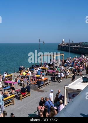 Live-Musik auf Folkestone Harbour Arm, Kent, mit Menschenmassen, die an einem sonnigen Feiertag das Meer genießen. Stockfoto