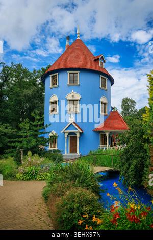 Naantali, Finnland - 27.07.2024: Ein lebendiger blauer Turm mit einem roten konischen Dach, umgeben von üppigem Grün in Moomintrolls Welt, Naantali, Finnland. Stockfoto