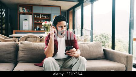 Glücklicher Mann, Kopfhörer oder Hören mit dem Telefon auf dem Sofa für Audio-Streaming oder Musik zu Hause. Männliche Person, Benutzer oder Lächeln mit Smartphone oder App Stockfoto