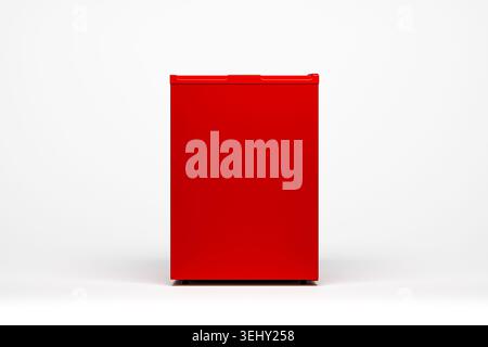 Ein eleganter roter Minikühlschrank steht vor einem sauberen weißen Hintergrund und zeigt sein kompaktes Design und leuchtende Farben, perfekt für kleine Räume. Stockfoto