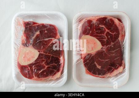 Zwei frische Stücke rohes Rindfleisch auf dem Knochen Ossobuco, verpackt in transparenter Folie auf einem weißen Tablett. Natürliche Fleischtextur mit Marmorierung und Knochenmark, CON Stockfoto