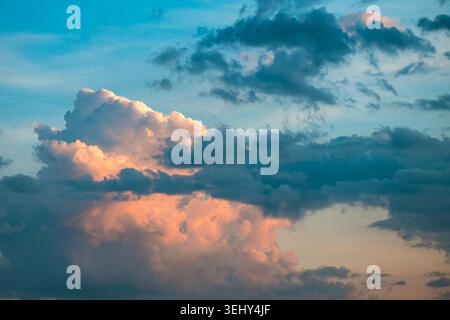 Wehende Cumulus-Wolken fangen die letzten Sonnenstrahlen ein und schaffen eine dramatische und farbenfrohe Atmosphäre vor einem Farbverlauf aus blauem und dunklem Himmel Stockfoto