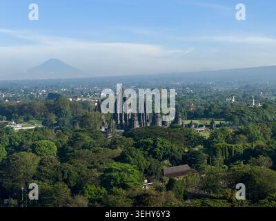 Blick aus der Vogelperspektive auf den Prambanan Tempelkomplex umgeben von üppigem tropischem Wald mit dem Vulkan Mount Merapi im Hintergrund Kecamatan Prambanan, Daerah ist Stockfoto