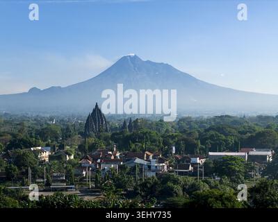 Blick aus der Vogelperspektive auf den Prambanan Tempel mit dem Berg Merapi im Hintergrund, umgeben von üppigem Grün und Wohndächern in Kecamatan Prambanan, Daer Stockfoto