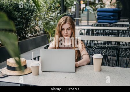 Frau tanzt auf Laptop-Computer, während sie am Kaffeetisch im Freien sitzt. Freischaffender Autor Blogger, unabhängiger Auftragnehmer, Online-Terrasse. Stockfoto