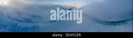 Aus der Vogelperspektive auf den Babusar Pass mit schneebedeckten Berggipfeln, einer gewundenen Straße durch das Tal und nebeligen Wolken in Naran, KPK, Pakistan. Stockfoto