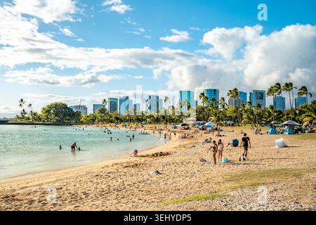 Sonnenanbeter und Familien genießen einen Sommertag am Sandstrand des Ala Moana Beach Park mit Honolulu Wolkenkratzern im Hintergrund Stockfoto