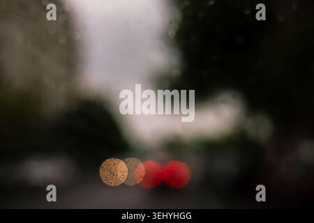 Regen fällt auf ein Autofenster mit verschwommenem Stadtverkehr und leuchtenden roten und gelben Lichtern Moody Urban wetterfest, das den verregneten, düsteren Herbsttag A festnimmt Stockfoto