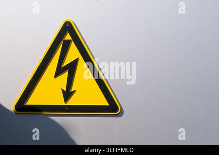 Nahaufnahme eines Warnschilds für Hochspannungsgefahr mit gelbem Blitzsymbol an einem Maschendrahtzaun. Konzept für elektrische Gefahren, Stromversorgung Stockfoto