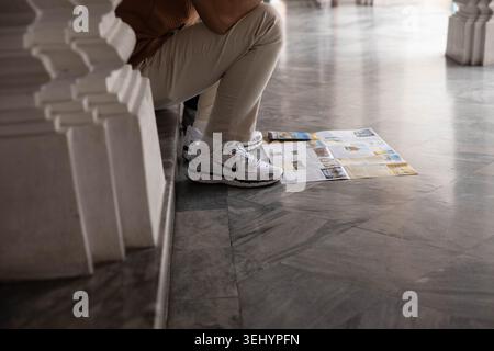 BANGKOK, THAILAND-16. MAI 2026: Mann in weißen Sneakers, der auf dem Boden liegt und eine Reisekarte liest, Nike Sneakers, Hochwinkelansicht Stockfoto