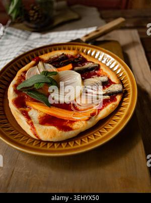 Vertikale Aufnahme einer frischen, knusprigen und duftenden Pizza mit herzhaften Sardellen, geschnittenen Zwiebeln und lebendigem Gemüse Stockfoto