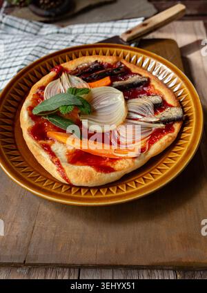 Vertikale Aufnahme einer frischen, knusprigen und duftenden Pizza mit herzhaften Sardellen, geschnittenen Zwiebeln und lebendigem Gemüse Stockfoto