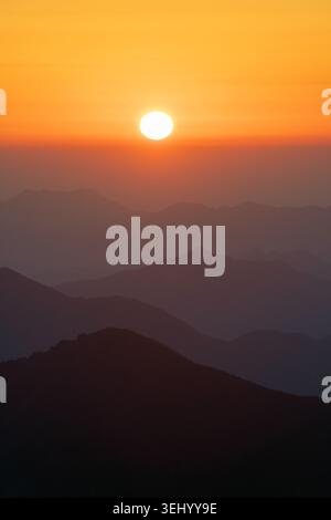 Blick auf den Sonnenaufgang über den geschichteten Silhouetten der Gipfel des Gelben Berges unter einem leuchtenden orangefarbenen Himmel Huangshan City, Anhui, China. Stockfoto