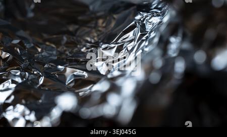 Kontrastreiche Makroaufnahme aus zerknitterter Silberfolie mit metallischen Glanzlichtern und Schatten Stockfoto