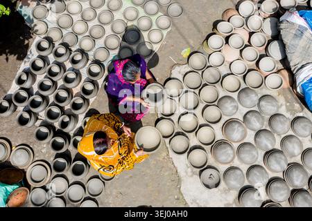 Munshiganj, Bangladesch - 28. September 2021: Aus der Vogelperspektive zweier Frauen in farbenfrohen Saris, die handgemachte Tontöpfe auf dem Boden anordnen, um in der Sonne zu trocknen. Stockfoto