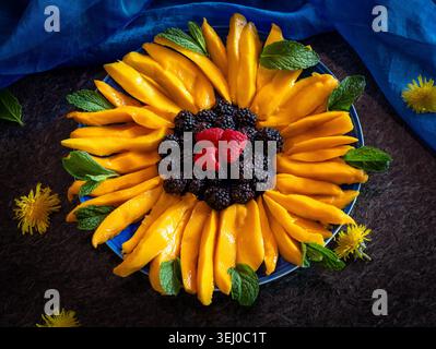 Eine optisch atemberaubende und gesunde Obstplatte in Form einer Sonnenblume angeordnet. Die künstlerische Präsentation zeigt lebendige Mangobeigen als Blütenblätter, Stockfoto