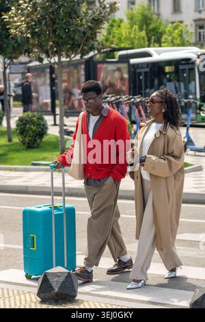 Stilvolles afroamerikanisches Ehepaar, Mann und Frau, die auf der Straße mit Koffer zum Hotel laufen. Stockfoto