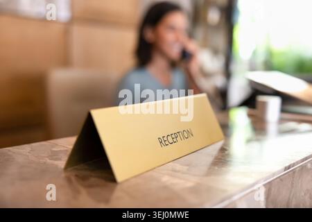 Schild an der Rezeption mit verschwommenem Hotelpersonal, Nahaufnahme Stockfoto
