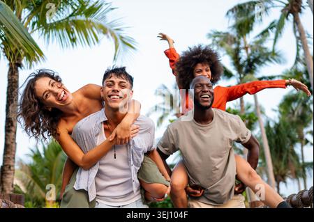 Verschiedene junge Freunde genießen Huckepack-Fahrten auf einer tropischen Brücke während des Sommerurlaubs Stockfoto