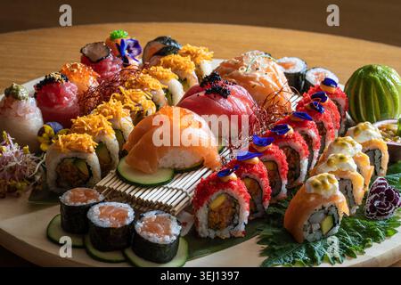 Eine vielfältige Auswahl an Sushi-Brötchen und Nigiri, kunstvoll auf einer runden Platte angeordnet, garniert mit bunten Belägen und essbaren Blumen. Stockfoto