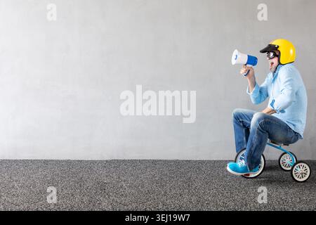 Senior Mann, der mit Kinderfahrrad fährt. Porträt eines lustigen Geschäftsmannes in voller Länge vor Betonwand mit Kopierraum. Unternehmensgründungskonzept Stockfoto