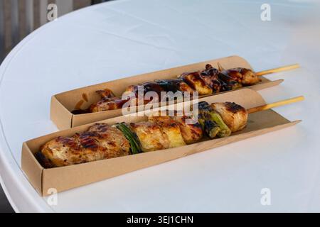 Nahaufnahme gegrillter Hähnchenspieße mit glasierter Sauce und Gemüse, serviert auf weißem Tisch im Freien. Stockfoto