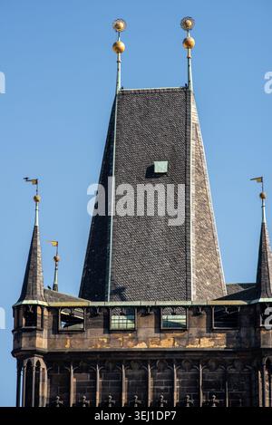 Blick aus der Nähe auf einen historischen Kirchturm mit dunklem Schieferdach, kleinen Türmen und goldenen Ornamenten vor einem klaren blauen Himmel. Stockfoto