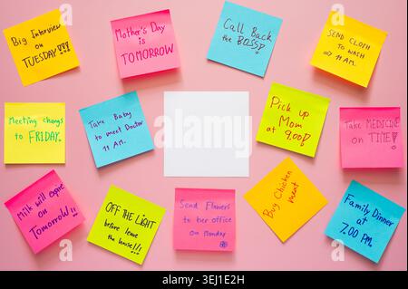 Farbenfrohe Haftnotizen mit handgeschriebenen Aufgaben auf weichem rosa Hintergrund mit einer zentralen leeren Notiz. Stockfoto