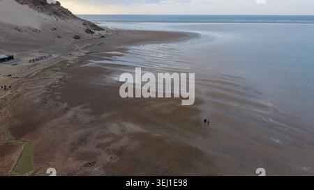 Aus der Vogelperspektive auf einen breiten, leeren Strand mit Ebbe, ruhigem Meer, Sandstrand und kleinen Leuten, die in der Nähe des Wassers spazieren Stockfoto