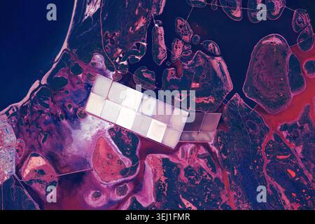Abstrakte Satellitenansicht von Küstensalzverdunstungsteichen und violetten Feuchtgebieten. Farbenfrohe geometrische Gittermuster von Salzpfannen im Kontrast zu natürlichem o Stockfoto