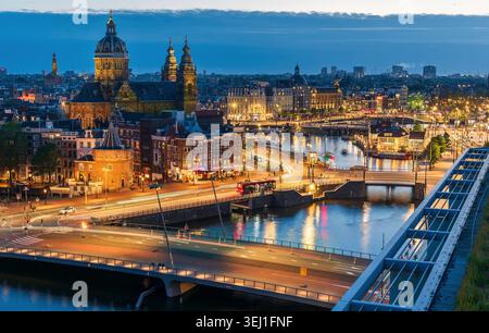 Amsterdam, Niederlande, 16. Mai 2026: Luftansicht der Stadt zur blauen Stunde mit beleuchteter Architektur, Brücken und dem Fluss Amstel, der sich in der Stadt widerspiegelt Stockfoto