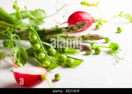Frische grüne Erbsenschoten mit Sprossen, Rettich und grünem Spargel auf weißem hölzernem Hintergrund. Konzept der gesunden Ernährung, frisches Gemüse. Stockfoto