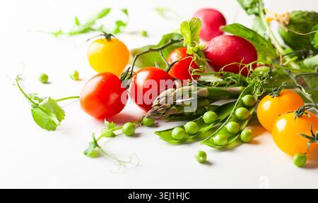 Frische grüne Erbsenschoten mit Sprossen, Rettich, Tomaten und grünem Spargel auf weißem hölzernem Hintergrund. Konzept der gesunden Ernährung, frisches Gemüse. Stockfoto