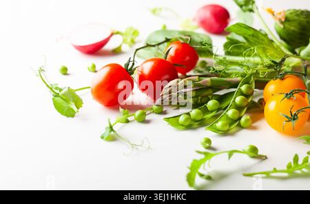 Frische grüne Erbsenschoten mit Sprossen, Rettich, Tomaten und grünem Spargel auf weißem hölzernem Hintergrund. Konzept der gesunden Ernährung, frisches Gemüse. Stockfoto