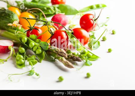Frische grüne Erbsenschoten mit Sprossen, Rettich, Tomaten und grünem Spargel auf weißem hölzernem Hintergrund. Konzept der gesunden Ernährung, frisches Gemüse. Stockfoto