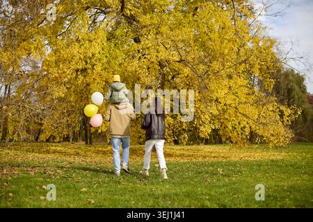 Glückliche Familie spazieren im Herbstpark mit Tochter und Ballons unter goldenen Bäumen Stockfoto