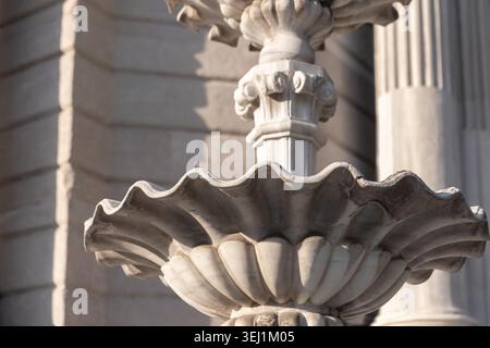 Das reich verzierte Steinbrunnenbecken wurde aus nächster Nähe erfasst und hebt geschnitzte, gewellte Kanten, verwitterte Textur und klassische architektonische Details in weicher Natur hervor Stockfoto