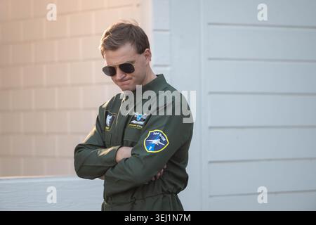 Selbstbewusster männlicher Pilot im grünen Fluganzug mit Pilotensonnenbrille, stehend mit überkreuzten Armen im Freien, repräsentiert Professionalität, Karriere und Führung in der Luftfahrt Stockfoto