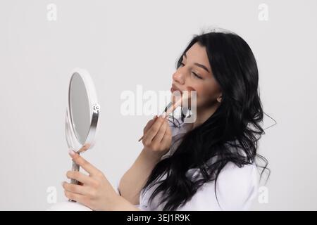 Junge Frau, die in einen Handspiegel schaut und Make-up aufträgt Stockfoto