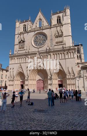 Vertikaler Flachwinkelblick auf die gotische Fassade der Kathedrale Saint Jean mit Touristen auf dem Kopfsteinpflasterplatz in Lyon, UNESCO-Stätte, Frankreich. Stockfoto