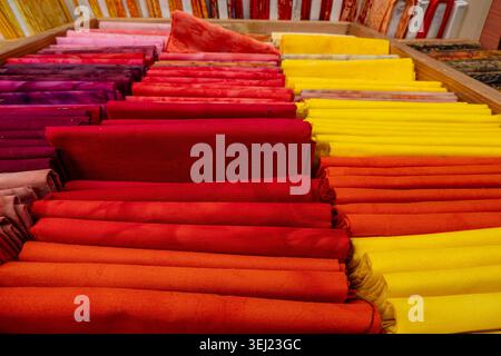 In Reihen angeordnete Stoffmuster zeigen einen Farbverlauf in Gelb, Rot und Lila und heben eine Textilkollektion mit verschiedenen Mustern und hervor Stockfoto