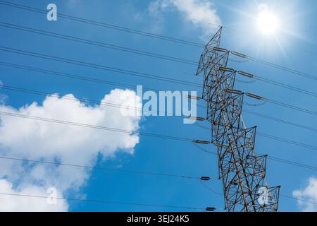 Hochspannungsturm steht hoch am Himmel. Sonnenlicht leuchtet von Metalllinien, die sich weit ausdehnen. Das Stromnetz verbindet Städte mit standhafter Stärke. E Stockfoto