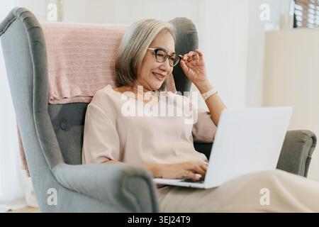 Ältere Frau mit Laptop-Computer Sitzen Entspannen Sie sich zu Hause Genießen Sie glückliches Lächeln, ältere Frau genießt mit moderner Technologie. Stockfoto