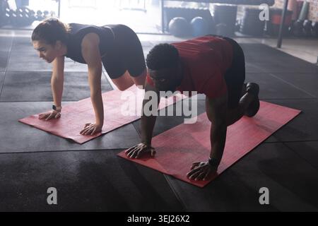 Verschiedene Workout-Partner führen Plank Kniestücken auf roten Matten mit Handgelenkstracker in Sportbekleidung durch Stockfoto