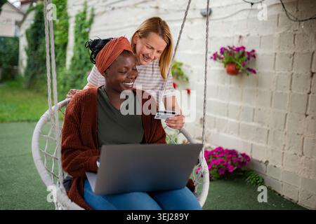 Weibliche Freunde, die Online-Shopping mit Kreditkarte und Laptop genießen Stockfoto