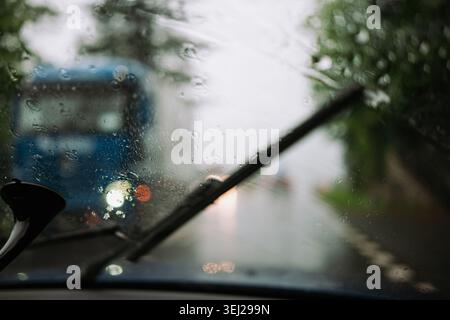 Ein Blick aus dem Inneren eines Fahrzeugs durch eine nasse Windschutzscheibe, die bei schlechtem Wetter von Regentropfen bedeckt ist, und zeigt, dass ein Wischerblatt die Scheibe reinigt und ein Stockfoto