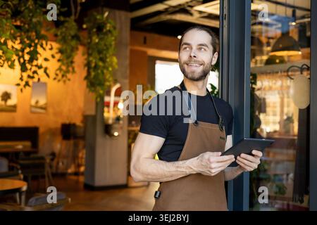 Fröhlicher Angestellter blickt weg, während er das Tablet hält Stockfoto