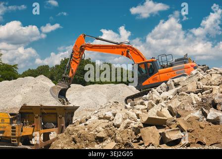 Abriss: Ein orangener Bagger bewegt Schutt auf einer Baustelle mit blauem Himmel Stockfoto