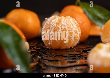 Reife, saftige und geschälte Mandarinen liegen auf einer glänzend schwarzen Oberfläche, bedeckt mit klaren Wassertropfen, frischen weichen und süßen Mandarinen auf einem schwarzen Glas Stockfoto