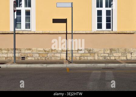 Stange mit leerem Richtungsschild auf dem Gehweg. Fassade aus Putz und Steinen mit zwei Fenstern. Stadtstraße vor dem Hotel. Hintergrund für Kopierbereich Stockfoto